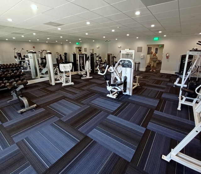 exercise room featuring a paneled ceiling, baseboards, dark colored carpet, and recessed lighting