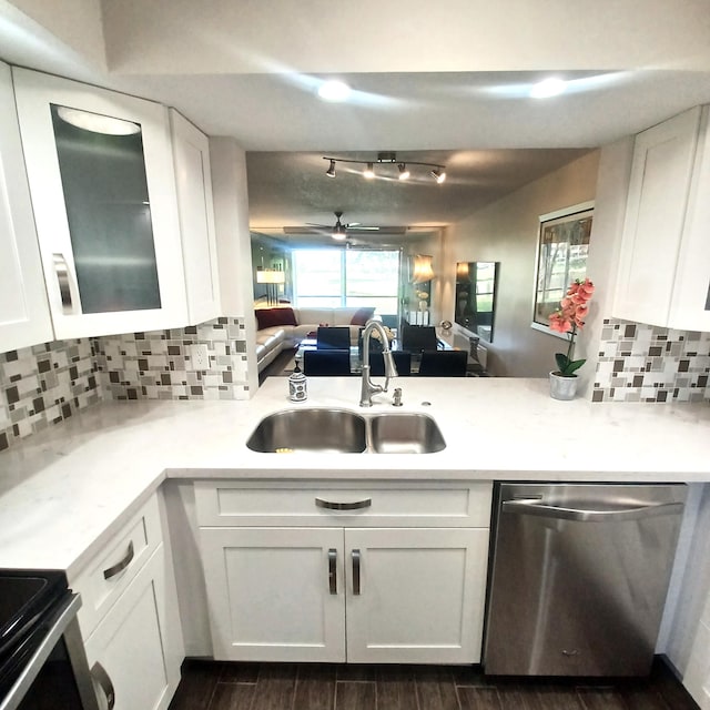 kitchen with white cabinets, glass insert cabinets, open floor plan, stainless steel dishwasher, and a sink