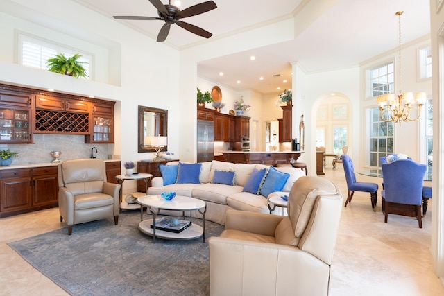 living room with crown molding, ceiling fan with notable chandelier, and a high ceiling