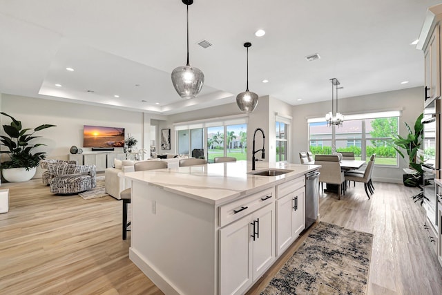 kitchen with an island with sink, stainless steel appliances, sink, decorative light fixtures, and white cabinets