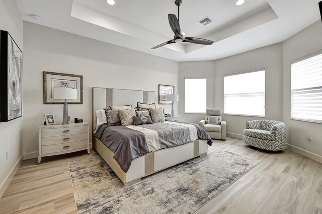 bedroom with ceiling fan, a tray ceiling, and light hardwood / wood-style flooring