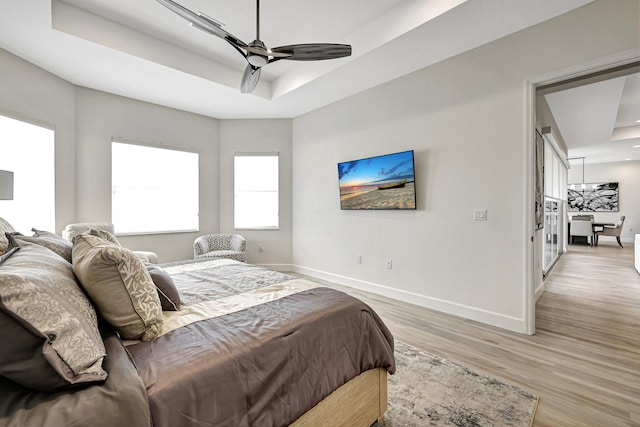 bedroom with ceiling fan, a tray ceiling, and light wood-type flooring