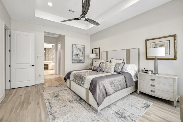 bedroom with ensuite bathroom, a tray ceiling, light hardwood / wood-style floors, and ceiling fan