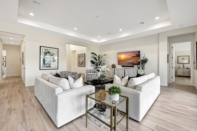 living room with light hardwood / wood-style floors and a raised ceiling