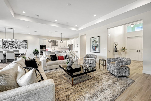 living room featuring a chandelier, light wood-type flooring, and a raised ceiling