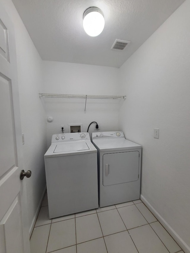 laundry area with washer and dryer, a textured ceiling, and light tile patterned floors