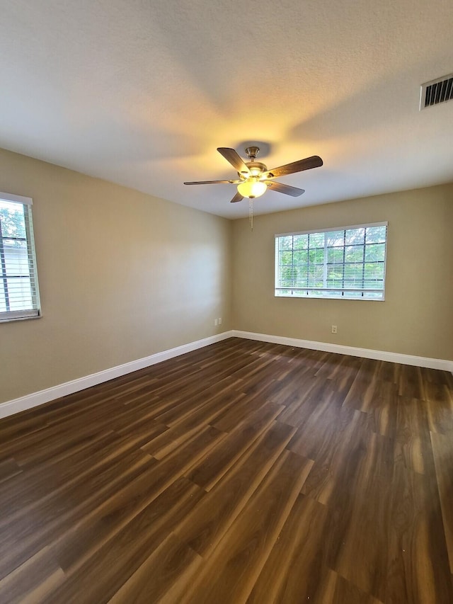 spare room featuring a textured ceiling, dark wood-type flooring, plenty of natural light, and ceiling fan