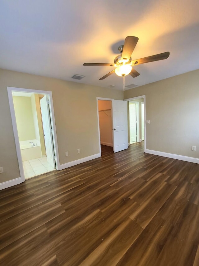 unfurnished bedroom featuring ceiling fan, dark hardwood / wood-style flooring, a spacious closet, connected bathroom, and a closet