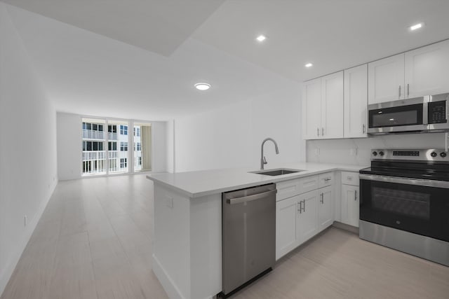 kitchen with stainless steel appliances, sink, kitchen peninsula, and white cabinets