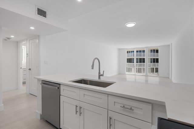 kitchen with sink, white cabinetry, light hardwood / wood-style floors, stainless steel dishwasher, and light stone counters