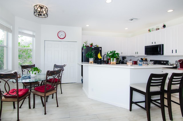 kitchen featuring an inviting chandelier, black appliances, tasteful backsplash, white cabinetry, and light hardwood / wood-style flooring