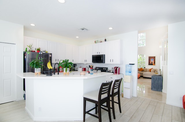 kitchen with white cabinets, a kitchen bar, black appliances, and a kitchen island