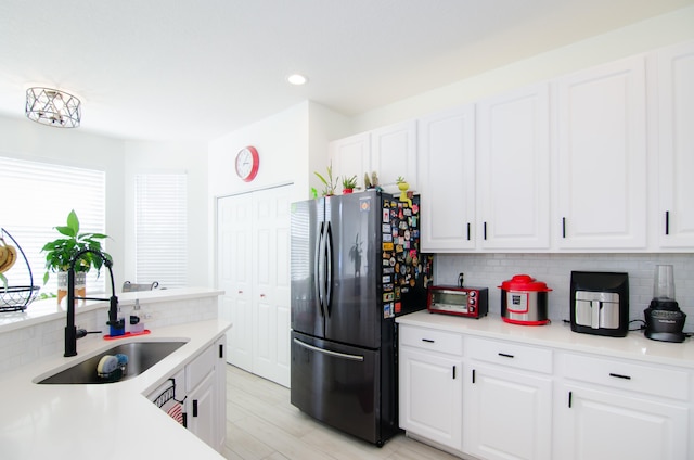 kitchen with sink, backsplash, white cabinets, stainless steel fridge, and light wood-type flooring