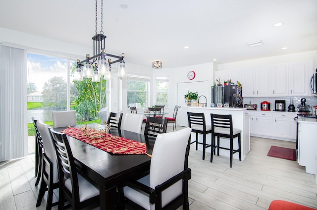 dining room with light wood-type flooring, a wealth of natural light, sink, and an inviting chandelier