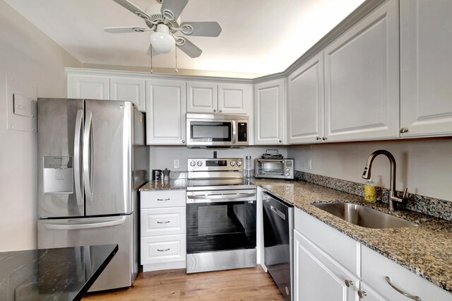 kitchen with appliances with stainless steel finishes, sink, light hardwood / wood-style floors, white cabinets, and dark stone countertops