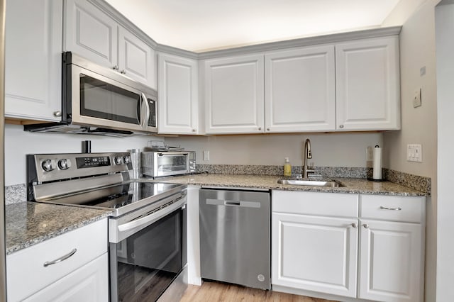 kitchen with sink, appliances with stainless steel finishes, white cabinetry, and light hardwood / wood-style floors