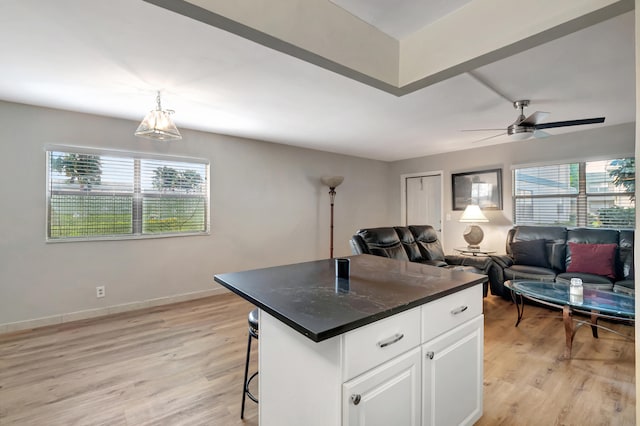 kitchen with a kitchen island, a breakfast bar, hanging light fixtures, white cabinets, and light hardwood / wood-style flooring