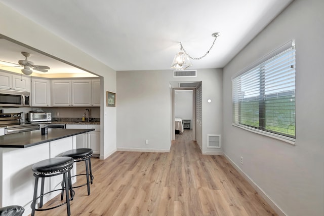 kitchen with hanging light fixtures, white cabinets, appliances with stainless steel finishes, light hardwood / wood-style floors, and ceiling fan