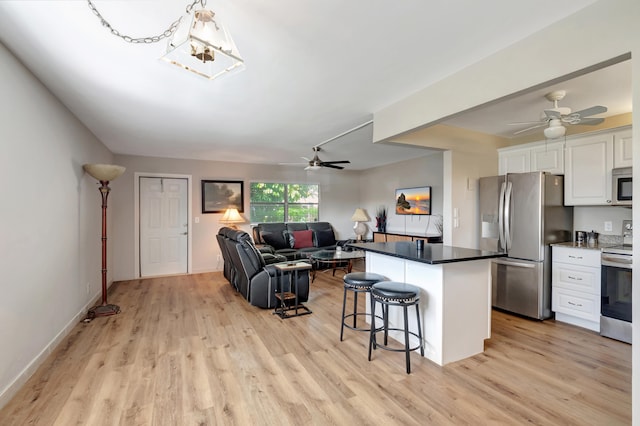 kitchen with ceiling fan, light hardwood / wood-style floors, stainless steel appliances, white cabinets, and a breakfast bar area