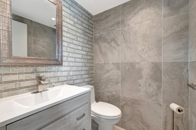 bathroom featuring toilet, vanity, and tile walls