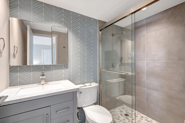 bathroom with a shower with door, toilet, tile walls, vanity, and tasteful backsplash