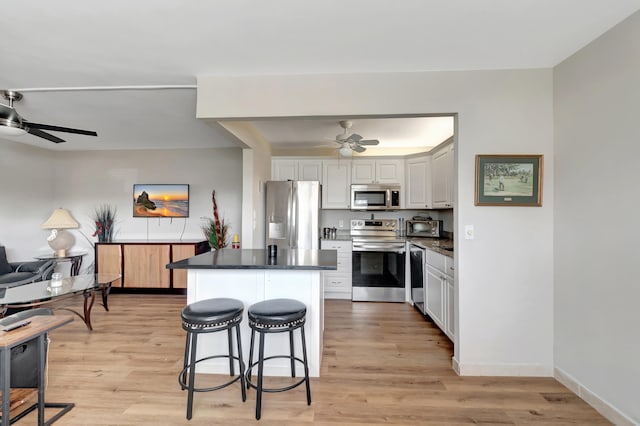 kitchen featuring stainless steel appliances, a breakfast bar, light wood-type flooring, white cabinetry, and ceiling fan