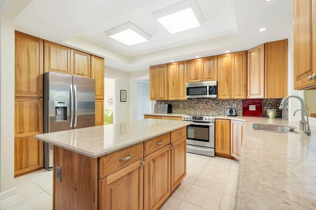 kitchen with a raised ceiling, appliances with stainless steel finishes, a kitchen island, light stone countertops, and sink