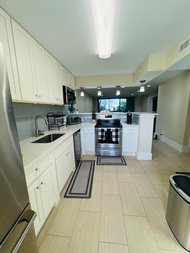 kitchen with appliances with stainless steel finishes, kitchen peninsula, white cabinets, and sink