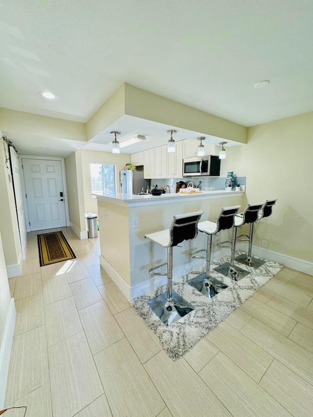 kitchen with appliances with stainless steel finishes, a breakfast bar, white cabinets, and kitchen peninsula