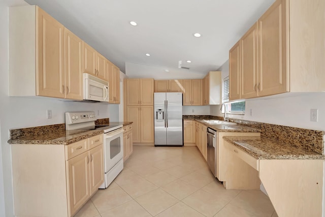 kitchen with light brown cabinetry, sink, appliances with stainless steel finishes, vaulted ceiling, and dark stone counters