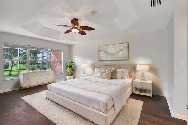 bedroom with a raised ceiling, ceiling fan, visible vents, baseboards, and dark wood-style flooring