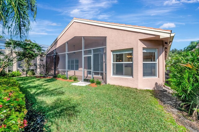 back of house with stucco siding, a yard, and a sunroom