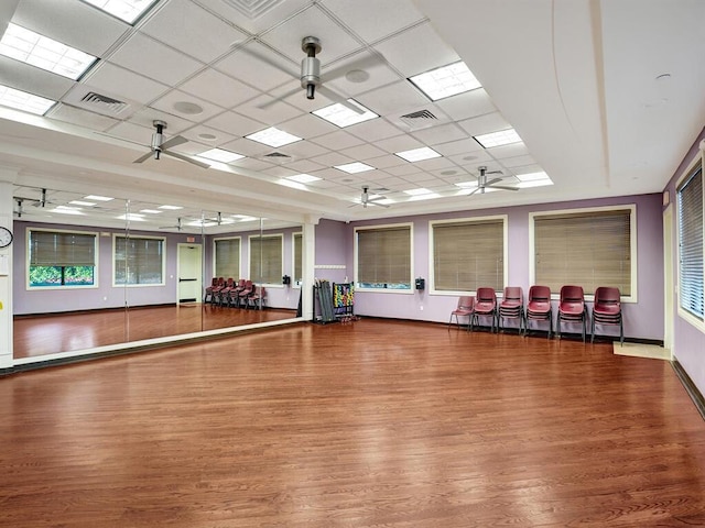 workout area with a paneled ceiling, wood finished floors, visible vents, and a ceiling fan