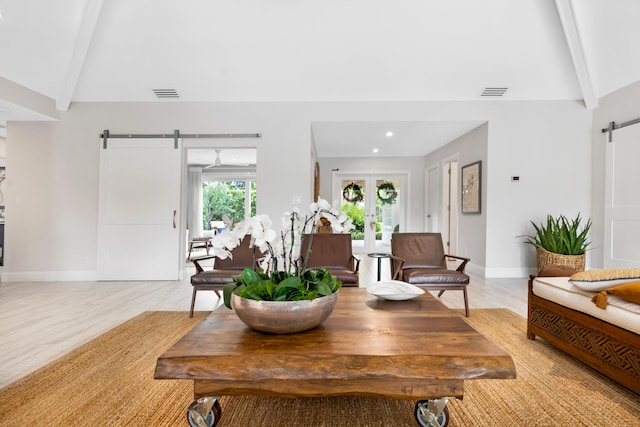 living room featuring light hardwood / wood-style flooring, french doors, a barn door, and lofted ceiling with beams