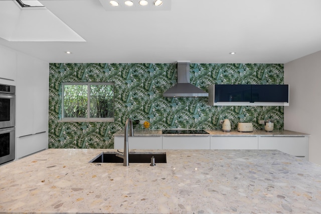 kitchen featuring wall chimney range hood, decorative backsplash, white cabinets, and sink