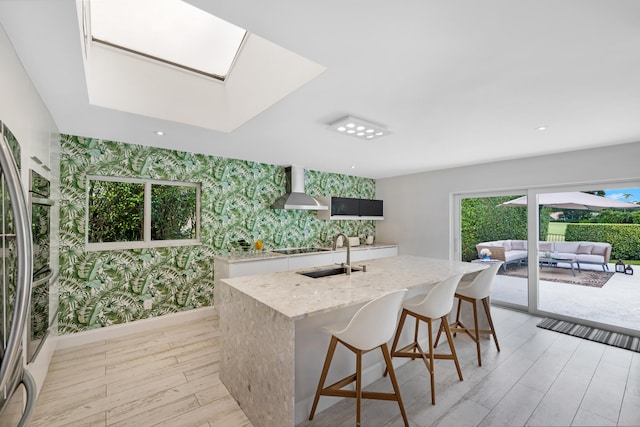 kitchen with wall chimney exhaust hood, a center island with sink, sink, white cabinetry, and light hardwood / wood-style floors