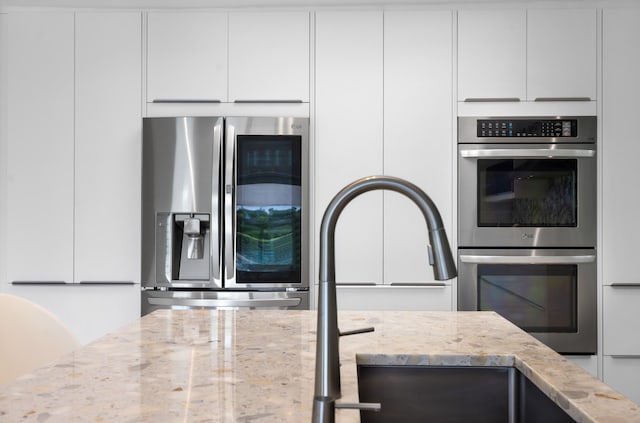 kitchen with appliances with stainless steel finishes, light stone counters, and white cabinetry