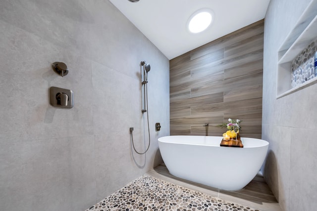 bathroom featuring tile walls, vaulted ceiling, tile patterned flooring, and a washtub