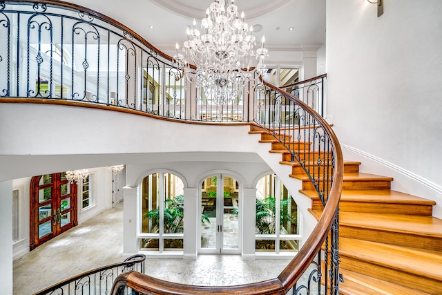 staircase featuring french doors, crown molding, an inviting chandelier, and a high ceiling