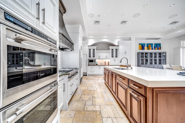 kitchen featuring decorative backsplash, sink, a center island with sink, and white cabinets