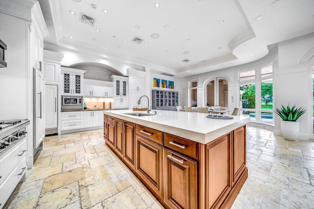 kitchen with white cabinets, a raised ceiling, an island with sink, stainless steel appliances, and sink