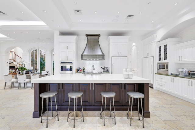 kitchen with tasteful backsplash, a kitchen bar, a large island, stainless steel appliances, and premium range hood