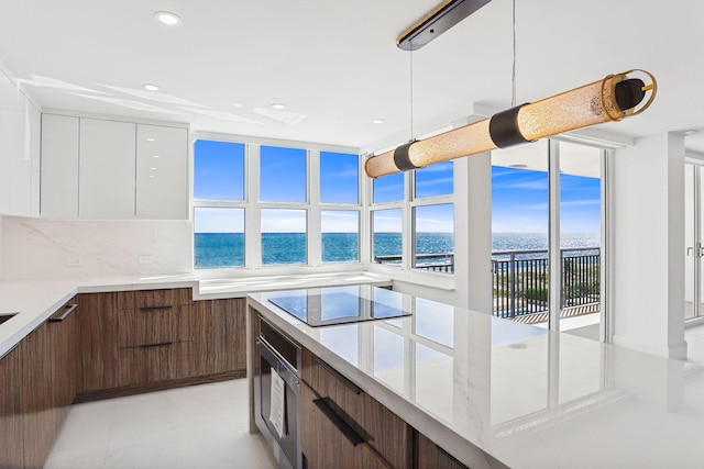 kitchen featuring black electric stovetop, tasteful backsplash, decorative light fixtures, white cabinets, and a water view