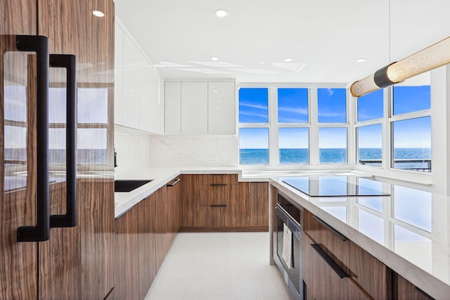 kitchen with decorative backsplash, stainless steel oven, white cabinetry, black electric stovetop, and a water view