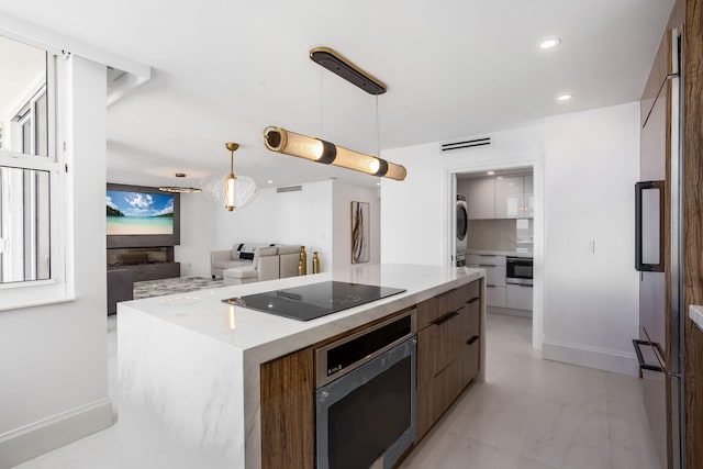 kitchen with oven, stacked washing maching and dryer, a center island, black electric stovetop, and decorative light fixtures