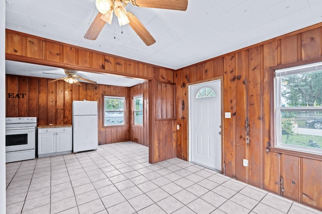 kitchen featuring wooden walls, light tile patterned floors, plenty of natural light, and white appliances