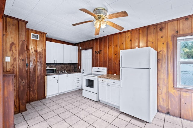 kitchen with white appliances, white cabinetry, ceiling fan, wooden walls, and decorative backsplash