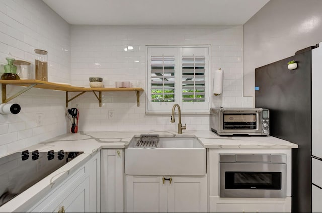 kitchen featuring decorative backsplash, black electric stovetop, sink, light stone countertops, and white cabinetry