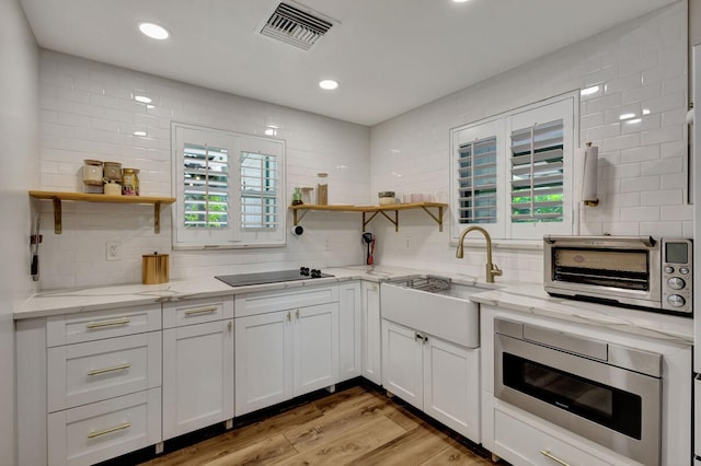 kitchen with stainless steel microwave, white cabinetry, light stone countertops, light wood-type flooring, and black electric cooktop