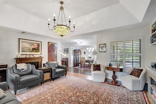 living room featuring vaulted ceiling, a raised ceiling, wood-type flooring, and an inviting chandelier